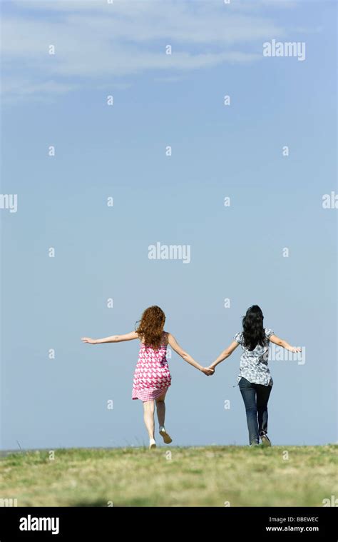 Two Young Women Walking Hand In Hand Outdoors Rear View Stock Photo