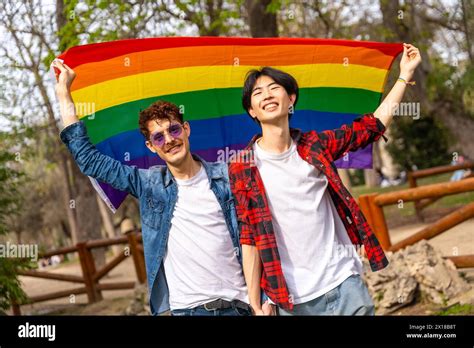 Portrait Of A Multi Ethnic Gay Couple Raising A Rainbow Lgbt Flag In A Park Stock Photo Alamy