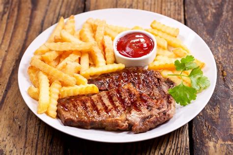 Plato De Carne A La Parrilla Con Papas Fritas En Mesa De Madera Foto