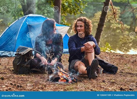 Young Hiker Couple Sitting And Talking While Warming Near A Campfire At