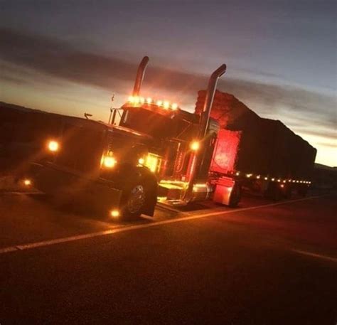 A Semi Truck With Its Lights On Driving Down The Road