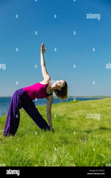 A yoga instructor demonstrates yoga poses during an outdoor yoga session in nature with blue ...