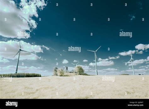 An Infrared Shot Of A Field With Wind Turbines And Trees Under The