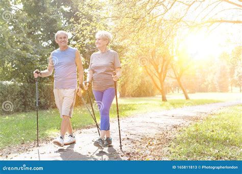 Photo Of Happy Senior Couple With Hiking Poles Walking In Park Stock