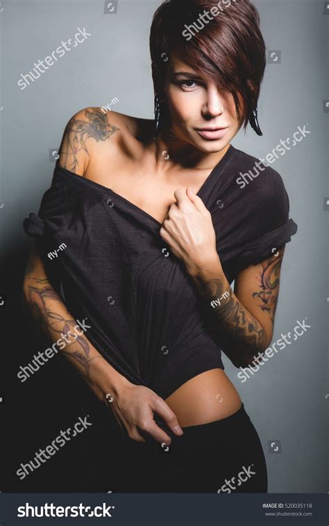 Beautiful Brunette Woman With Tattoos And A Sports Figure Posing On Dark Background In Studio