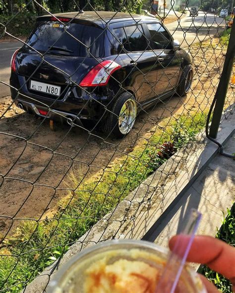 a person holding a drink in front of a car behind a chain link fence,