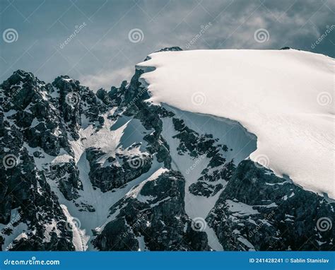 Bright Alpine Landscape With Snow Covered Mountain Top And Black Rocks