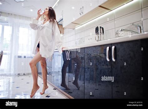 Elegante junge Frau im Bikini und männliche Shirt posiert mit einem Glas Wasser in der Küche