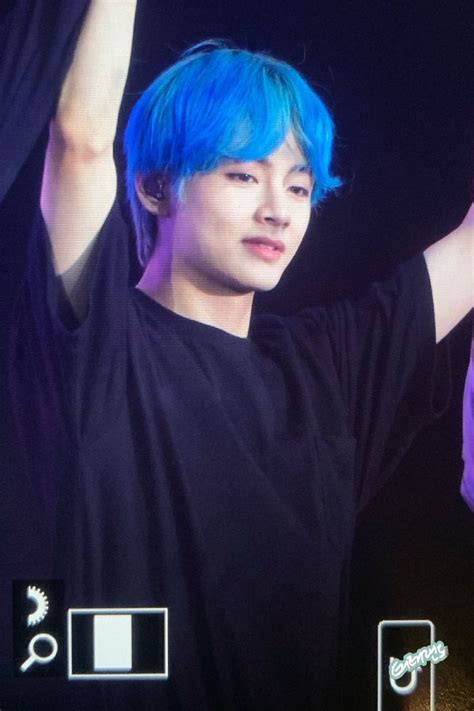 A Man With Blue Hair And Black Shirt Holding His Hands Up In The Air At