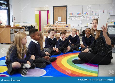 Female Teacher Holding Up a Book in Front of Her Class of Elementary School Kids Sitting on the ...