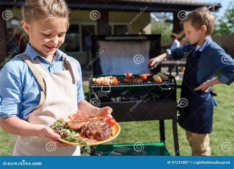 Girl In Apron Holding Plate With Fresh Steaks While Her Brother