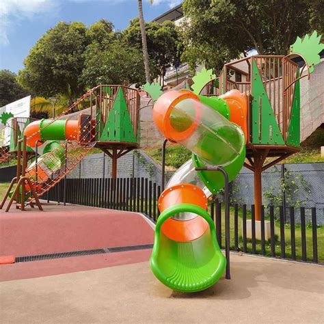 A Green And Orange Slide In The Middle Of A Play Area With Trees On It