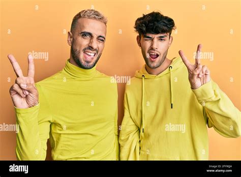 Homosexual Gay Couple Standing Together Wearing Yellow Clothes Smiling With Happy Face Winking