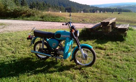 A Blue Motorcycle Parked On Top Of A Lush Green Field Next To A Wooden