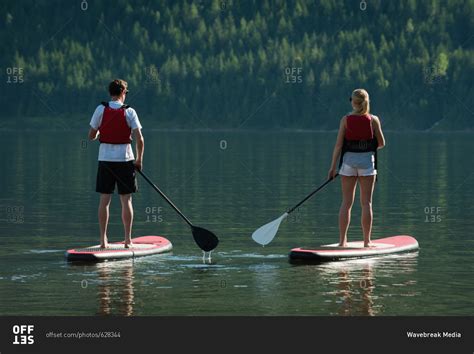 Couple doing stand up paddle boarding in river stock photo - OFFSET