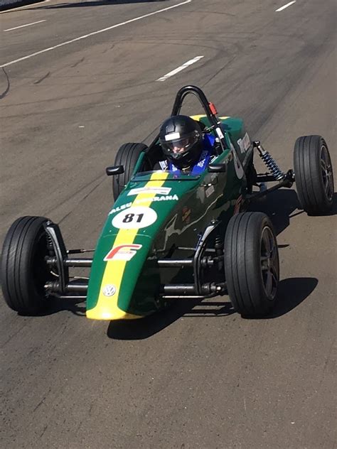 A Man Driving A Green And Yellow Race Car Down A Street