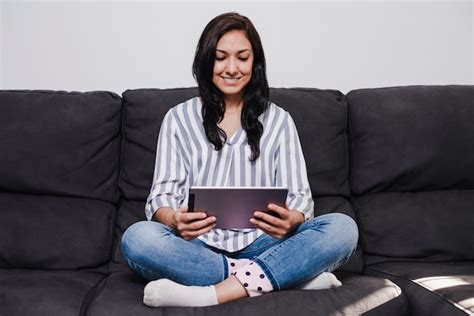 Joven latina sentada en el sofá leyendo en una tableta Foto Premium