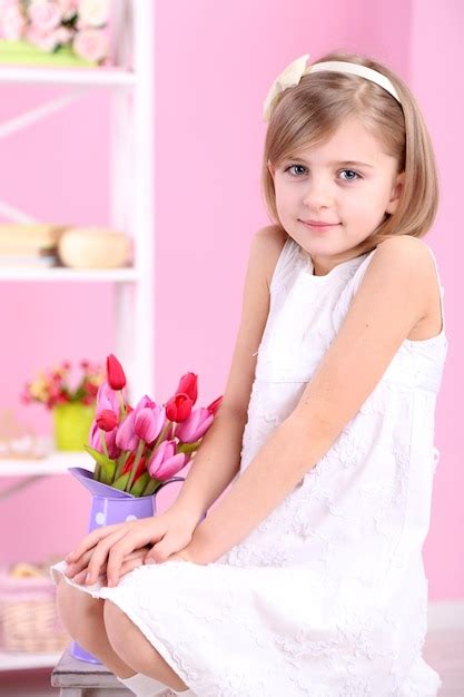 Niña sentada en una pequeña escalera con flores sobre fondo rosa Foto