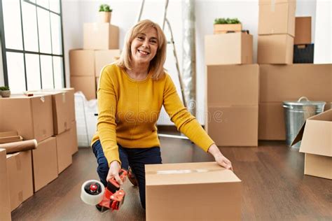 Middle Age Blonde Woman Packing Box Using Tape At New Home Stock Photo Image Of Adult Female
