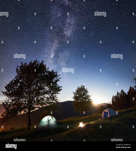 Tourist Camping Near Forest At Night Two Glowing Tents And Bonfire