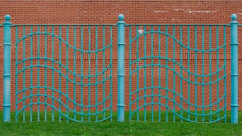 Aqua Blue Wavy Fence Built On Grassed Area With Red Brick Wall Behind