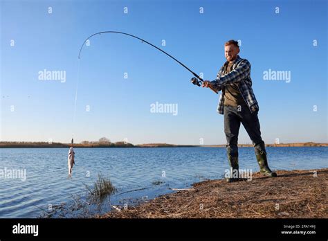 Fisherman Catching Fish With Rod At Riverside Stock Photo Alamy