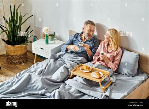 A Mature Loving Couple In Cozy Homewear Sitting On A Bed Embracing Each Other In A Tender