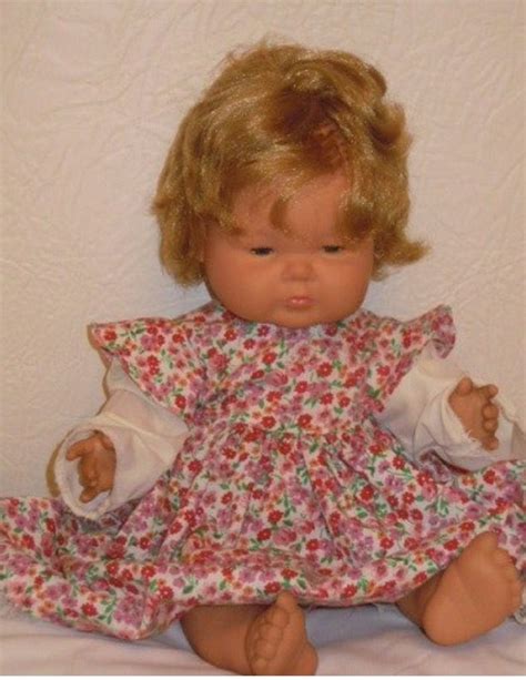 A Doll With Blonde Hair Sitting On Top Of A White Bed Next To A Wall