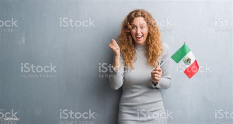 Young Redhead Woman Over Grey Grunge Wall Holding Flag Of Mexico