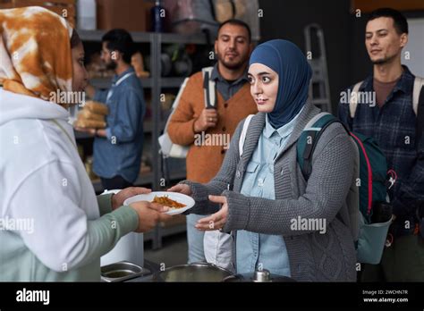 Waist Up Portrait Of Adult Middle Eastern Woman Wearing Hijab Taking Hot Meal At Refugee Help