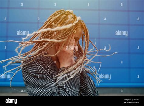 Dreads Shaking Lighthearted Teenage Girl In Front Of A Blue Panel Wall Covering She Is Wearing