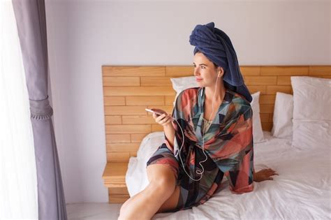 Free Photo Pretty Brunette Woman Wrapped In A Shower Towel Using Mobile Phone While Sitting On Bed