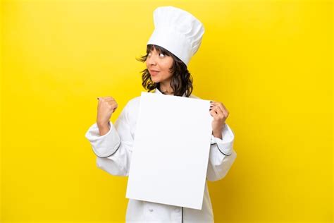 Mulher Latina Jovem Chef Isolada Em Fundo Amarelo Segurando Um Cartaz Vazio E Apontando O Lado