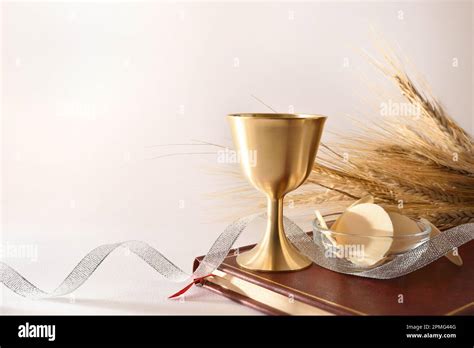 Cup Of Wine And Hosts On Bible For Eucharist On White Table With Silver