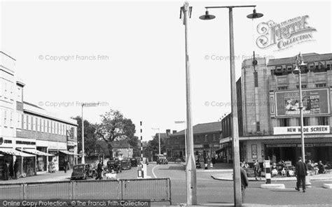 An Old Black And White Photo Of People Walking On The Sidewalk In Front