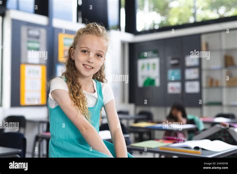 Caucasian Girl With Curly Blonde Hair Smiles In A School Classroom With Copy Space Stock Photo