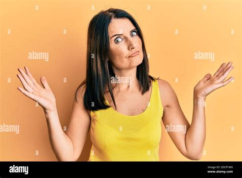 Middle Age Brunette Woman Wearing Casual Clothes Over Yellow Background Clueless And Confused