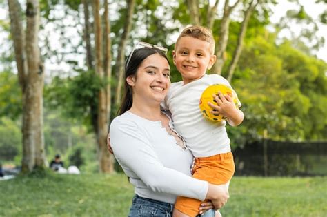 Belle Fille Latina Tenant Son Fils Tandis Que Le Garçon Tient Une Balle Dans Ses Mains Photo