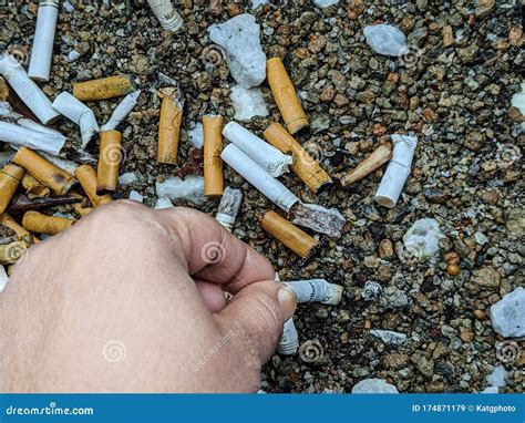 Persons Hand Putting Out Cigarette In A Pile Of Cigarette Butts Stock