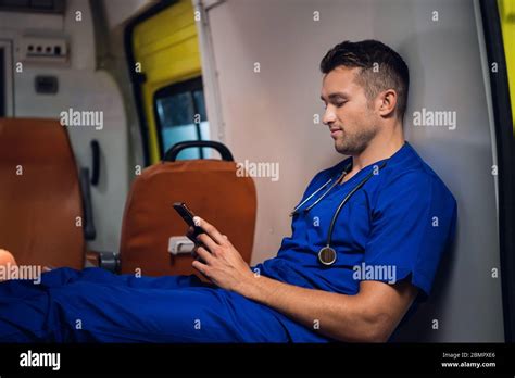 Male Paramedic In A Blue Uniform Resting And Browsing His Phone In The