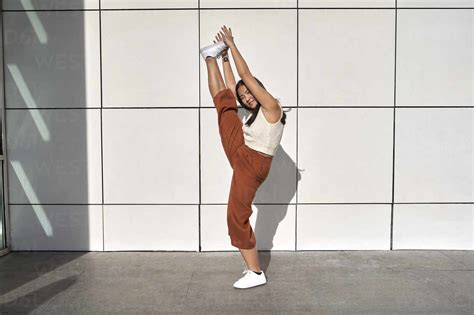 Young woman practicing standing splits against wall stock photo