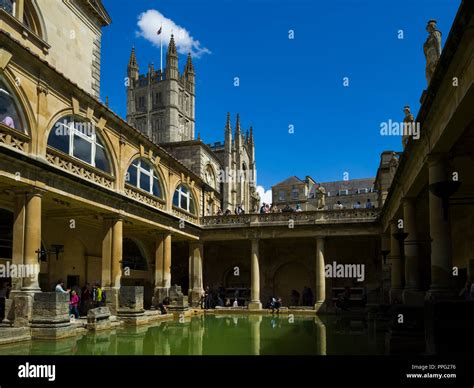 Visitors Exploring The Historic Roman Baths With Bath Abbey Towering Above Bath Somerset