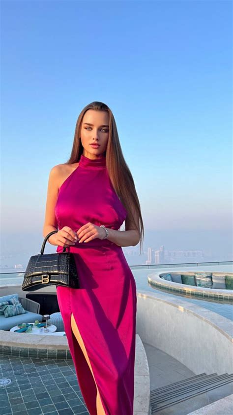 A Woman In A Pink Dress Is Standing Near The Water With Her Hand On Her Hip