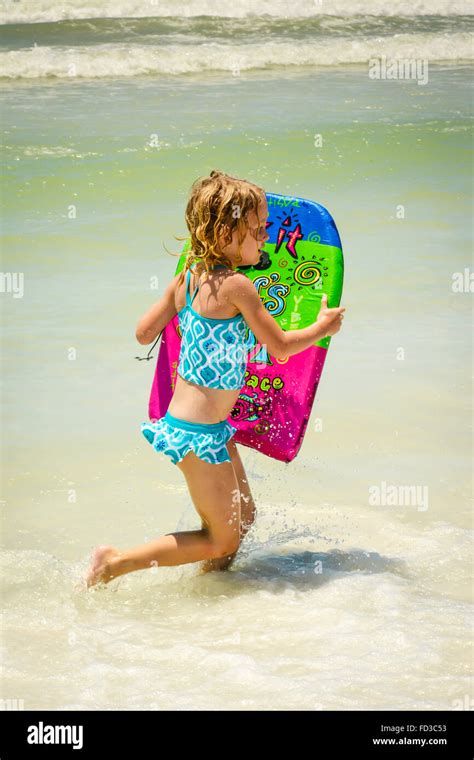 Junge blonde Mädchen im Badeanzug läuft in der Brandung entlang der Küste am Strand mit ihren