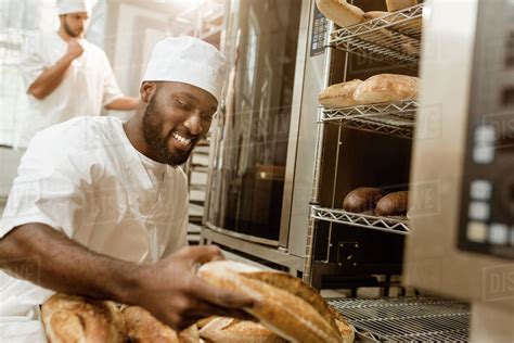 Happy African American Baker With Tray Of Fresh Loaves Of Bread On