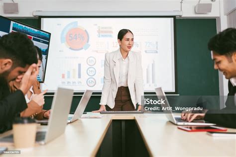 A Cheerful And Confident Asian Businesswoman Stands Present Bar Charts Data From Projector