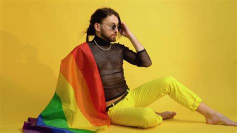 joven caucásico gay hombre 20s con arco iris a rayas bandera se sienta en amarillo antecedentes