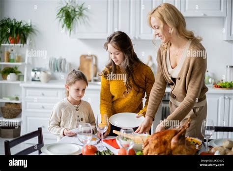 Smiling Blonde Woman Serving Table For Thanksgiving Dinner With Daughters In Kitchen Stock Image
