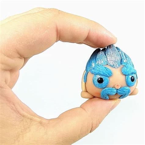 A Hand Holding A Tiny Doll With Blue Hair And Mustaches On It S Head