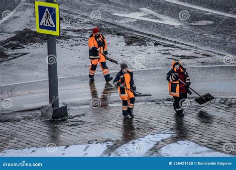 Women Workers In Orange Uniforms With Snow Shovels Walk Down The Street